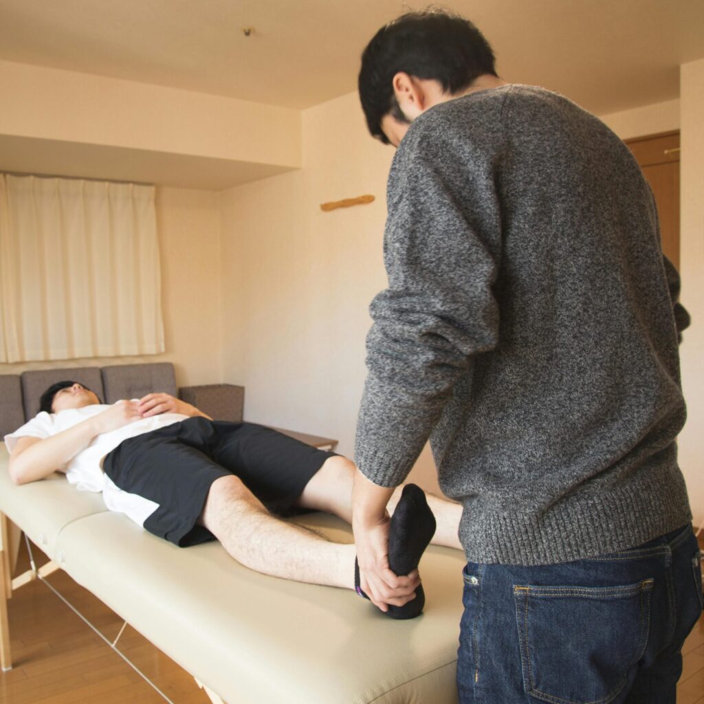 Male physiotherapist massaging legs to patient on couch and healing body while working at comfortable salon